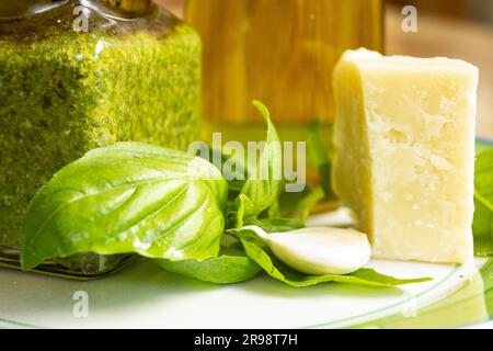 basilikum-Pesto in einem Becher in der Nähe der Zutaten für seine Zubereitung Stockfoto