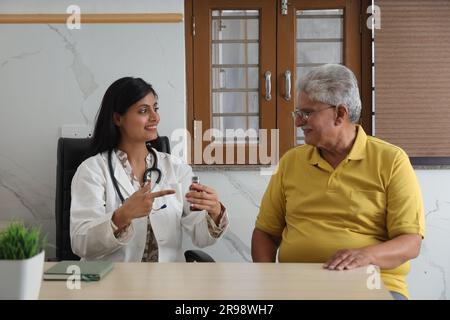 Attraktiver junger indischer Arzt, der mit einem Seniorenpatienten im Wohnzimmer eines Pflegeheims sitzt. Ein älterer Patient im Gespräch Stockfoto