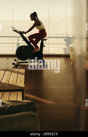 Frau demonstriert, wie ein Smart Bike die Fitness zu Hause verändert. Sportlerin trainiert zu Hause mit Leichtigkeit und erreicht ihre Gesundheits- und Fitnessziele Stockfoto