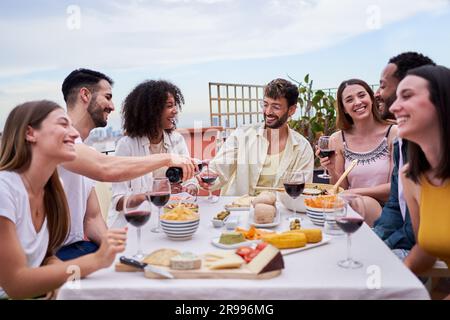 Multirassische Freunde, die tagsüber auf einem Dach zusammenkamen, essen und trinken. Wir haben Spaß zusammen. Stockfoto