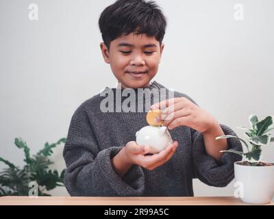 Ein Junge, der Münzen in ein Sparschwein steckt. Finanzielle Verantwortung lernen und Einsparungen prognostizieren. Einsparungskonzept. Investitionskonzept. Stockfoto