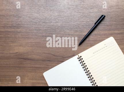 Blick auf einen hölzernen Schreibtisch von oben mit offenem Notizbuch und Stift. Leerer weißer Hintergrund mit Platz für Text. Draufsicht Stockfoto