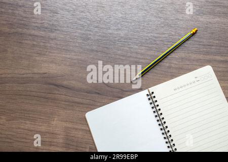 Blick auf einen hölzernen Schreibtisch von oben mit offenem Notizbuch und Stift. Leerer weißer Hintergrund mit Platz für Text. Draufsicht Stockfoto