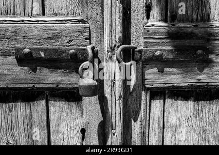 Nahaufnahme eines antiken Vorhängeschlosses in einer alten Holztür mit rauer, strukturierter Holzmaserung. Schwarzweißbild. Stockfoto