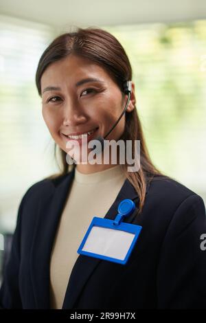 Lächelnde elegante Geschäftsfrau mit Abzeichen auf der Jacke, die ein Headset trägt Stockfoto