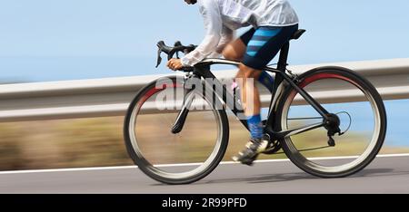 Bewegungsunschärfe eines Radrennens mit dem Fahrrad und dem Fahrer bei hoher Geschwindigkeit. Professionelle Radfahrerin in Rennkleidung während einer Radtour im Freien. Pann Stockfoto