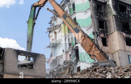Fassade eines verlassenen mehrstöckigen Wohngebäudes nach einem schweren Brand. Ein Baufachbagger mit einem Hydraulikbrecher zerstört ein Haus für Stockfoto