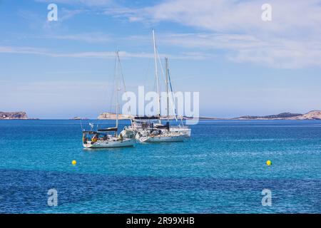 Eine atemberaubende Küstenlandschaft mit mehreren Booten, die nahe einer Küste unter dem blauen Himmel vor Anker liegen Stockfoto