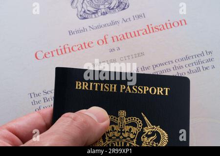 Hand mit britischem Reisepass neben dem Einbürgerungszertifikat als britischer Staatsbürger. Stafford, Großbritannien, 25. Juni 2023 Stockfoto