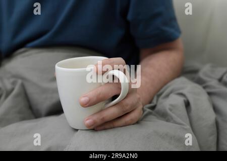 Ein Mann, der eine große Tasse auf dem Bett hält Stockfoto