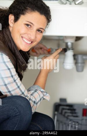 Fröhliche junge Frau, die ein undichtes Spülrohr in der Küche repariert Stockfoto
