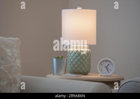 Nahaufnahme eines Holztisches mit einer Uhr mit weißem Gesicht und einer modernen Lampe Stockfoto