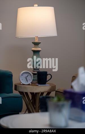 Eine beleuchtete Tischleuchte befindet sich auf einem kleinen, rustikalen Holztisch, daneben befindet sich eine dampfende Kaffeetasse Stockfoto