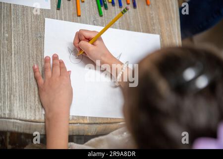 Eine junge Künstlerin sitzt am Schreibtisch und malt auf Papier Stockfoto