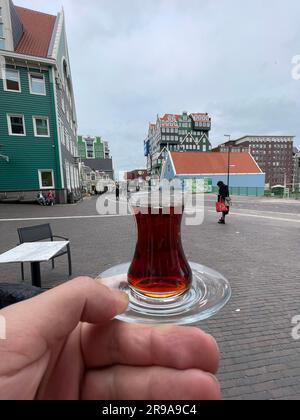 Zaandam, Niederlande - 13. Oktober 2021: Hand eines Mannes mit türkischem Tee vor dem ikonischen Gebäude des Inntel Hotel Zaandam in Zaandam, dem Nether Stockfoto