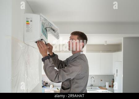 Ein Mann-Techniker, der in Uniform eine Klimaanlage in einer modernen Wohnung installiert. Stockfoto
