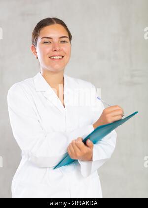 Eine Ärztin macht sich Notizen in Dokumenten, die eine Papiermappe in der Hand haben Stockfoto