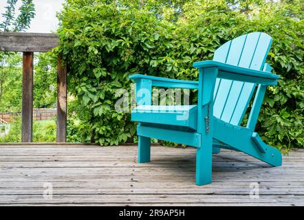 Leerer Adirondack-Stuhl auf einer hölzernen Hinterhofterrasse, Sommerlandschaft mit grüner Weinrebe Stockfoto