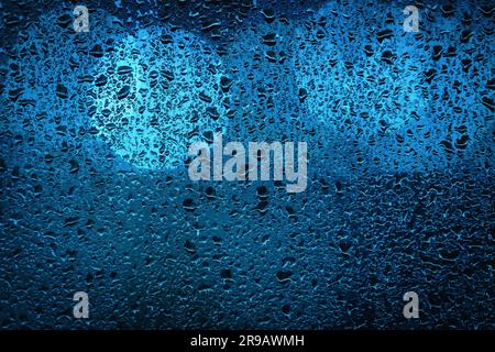 Blaue Bokeh Lichter hinter einem nassen Fenster auf einem regnerischen Abend in einer großen Stadt Stockfoto