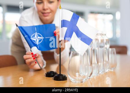 Die Sekretärin legt die Flaggen der NATO (OTAN) und Finnlands vor den Verhandlungen mit hochrangigen politischen Persönlichkeiten auf den Tisch Stockfoto