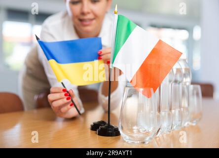 Vorbereitung auf Geschäftsverhandlungen - Frau setzt kleine Flaggen von Ländern der Ukraine und Italiens auf den Tisch Stockfoto