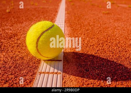 Gelber Tennisball berührt die Linie auf dem roten Tonplatz Stockfoto