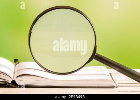 Lupe auf ein offenes Buch mit grünem Hintergrund Stockfoto