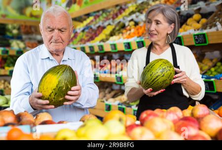 Dame im Gemüsehändler hilft dem alten Mann, Melone zu wählen Stockfoto