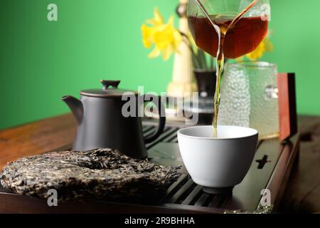 Ich gieße frisch gebrühten pu-erh-Tee in die Tasse auf dem Tisch, schließe die Tür Stockfoto