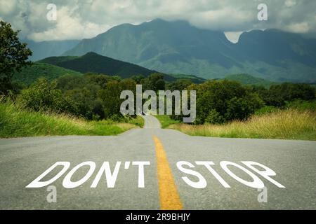 Motivationsausdruck. Worte hören nicht auf, geschrieben auf einer leeren Straße, die in die Berge führt Stockfoto