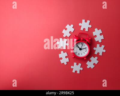 Roter Wecker mit weißem Puzzle auf rotem Hintergrund und Kopierbereich Stockfoto