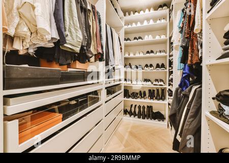 Ein begehbarer Kleiderschrank mit weißen Regalen und vielen Schuhen, die dahinter an der Wand hängen, Stockfoto