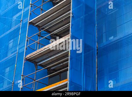 Gerüste an der Fassade eines Wolkenkratzers, Nahaufnahme eines Fotos. Baustelle mit blauem Sicherheitsnetz Stockfoto