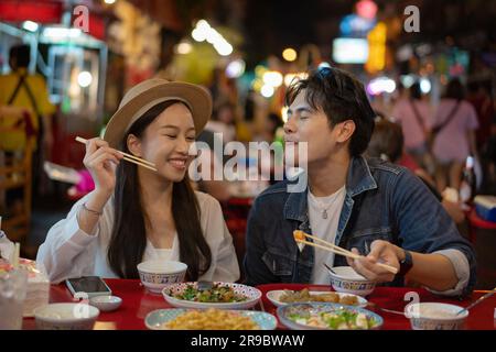 Junge asiatische Paartouristen, die gemeinsam thailändisches Street Food auf dem China Town Nachtmarkt in Bangkok in Thailand essen - Leute, die reisen, genießen das kulinarische Konzept Stockfoto