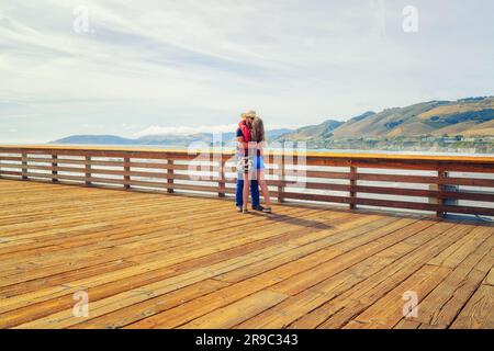 Pismo Beach, Kalifornien, USA - 3. Juni 2022. Junges Paar am Pier, grüne Hügel und wolkiger Himmelshintergrund. Pismo Beach Pier, California Central COA Stockfoto