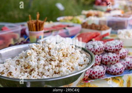 Ein Tisch voller Snacks. Eine Schüssel voller Mais im Vordergrund. Party im Freien. Picknick. Stockfoto