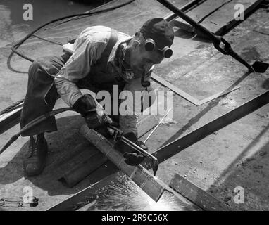 Vereinigte Staaten: c. 1938 Ein Arbeiter, der mit einem Acetylen-Sauerstoff-Brenner Winkeleisen schneidet. Stockfoto