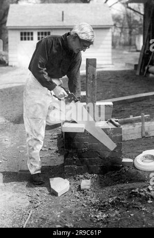 New York, New York: 1922 Schauspieler und Dramatiker Frank Bacon sägt ein Stück Holz in seinem Haus in Bayside in Queens auf Long Island. Stockfoto