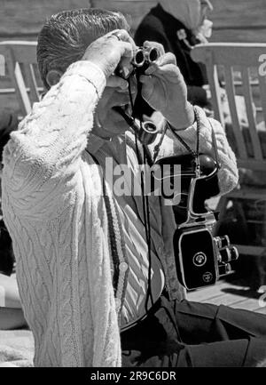 Alaska: ca. 1958. Ein Passagier auf dem kanadischen Kreuzfahrtschiff, Prince George, ist gut vorbereitet mit zwei Kameras, Ferngläsern und einer Pfeife, während er durch die Inside Passage von Vancouver nach Skagway fährt. Stockfoto