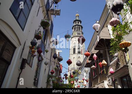 Die Reigerstraat mit bunten Laternen und Blick auf den 90 Meter hohen Abbey Tower de lange Jan in der niederländischen Stadt Middelburg. Blauer Himmel, Stockfoto