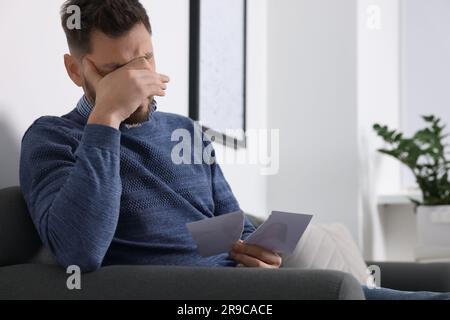 Ein weinender Mann, der ein zerrissenes Foto auf dem Sofa hält. Scheidungskonzept Stockfoto