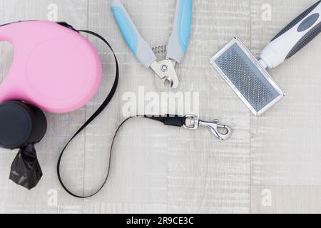 Rosafarbene einziehbare Hundeleine, Nagelschneider und Kammaufsatz auf Holzboden Stockfoto