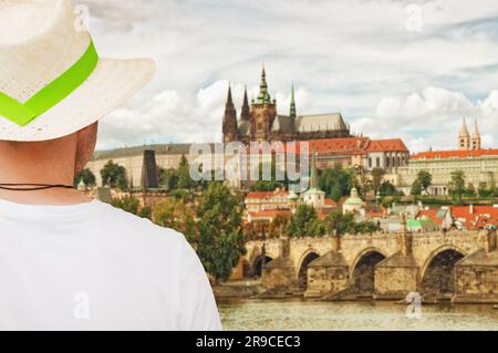 Tourist mit Strohhut in Prag, mit Blick auf die Burg Hradcany und die Karlsbrücke über der Moldau. Digitales Composite-Bild. Selektiver Fokus. Stockfoto