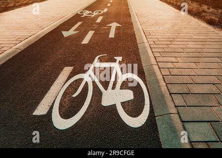 Asphaltfahrradweg mit Symbol für ein Fahrrad und Richtungspfeil bei Sonnenuntergang Stockfoto