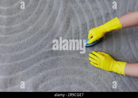 Reinheitskonzept und Reinigungskonzept - Draufsicht der Hände in gelben Gummihandschuhen Teppich mit Bürste reinigen, Kopierbereich über grauem Teppich Stockfoto