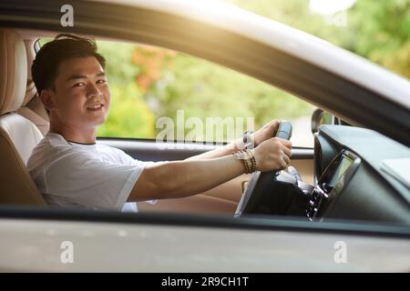 Glücklicher junger asiatischer Mann, der an einem sonnigen Tag Auto fährt Stockfoto