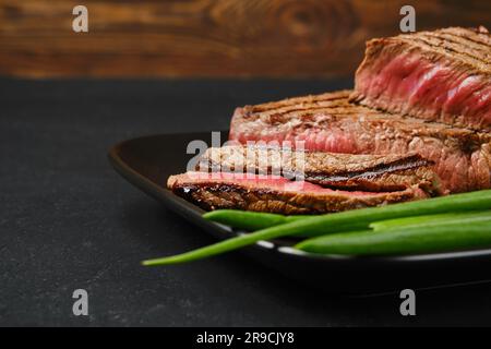 Nahaufnahme von gebratenen Rindersteaks, mittelgroß, mit frischem Gemüse auf schwarzem Hintergrund Stockfoto