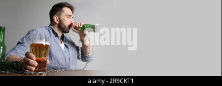 Er leidet an einem Kater. Mann mit alkoholischem Getränk am Tisch vor weißem Hintergrund angekettet, Platz für Text. Bannerdesign Stockfoto