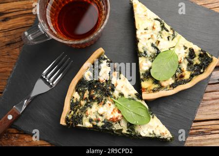 Leckere hausgemachte Spinatquiche, Tee und Gabel auf Holztisch, flach liegend Stockfoto