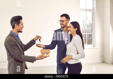 Immobilienmakler, der einem jungen, glücklichen, lächelnden Paar den Hausschlüssel gibt. Stockfoto
